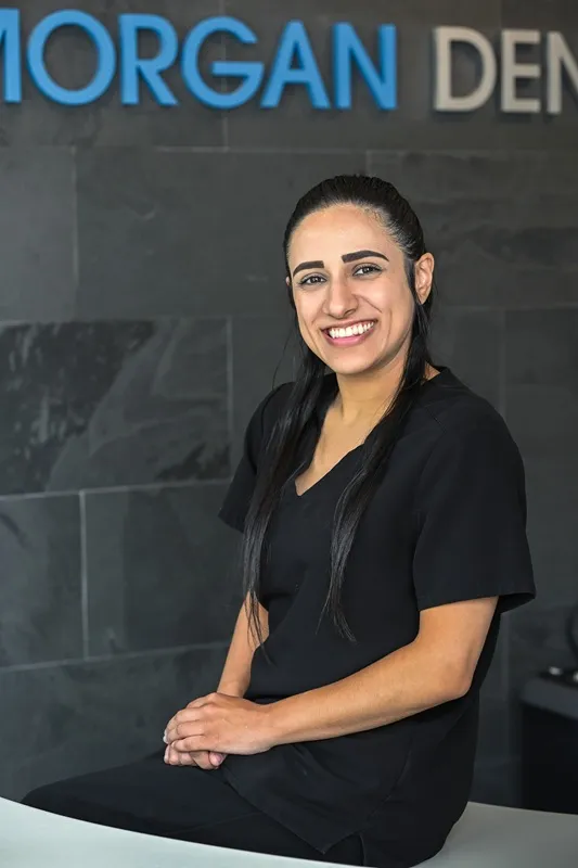 Jessica Pereira, Registered Dental Hygienist wearing dark scrubs smiling against a dark stone wall
