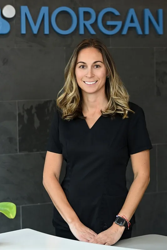 Melissa, Registered Dental Hygienist in dark scrubs smiling in front of a Morgan Dental sign